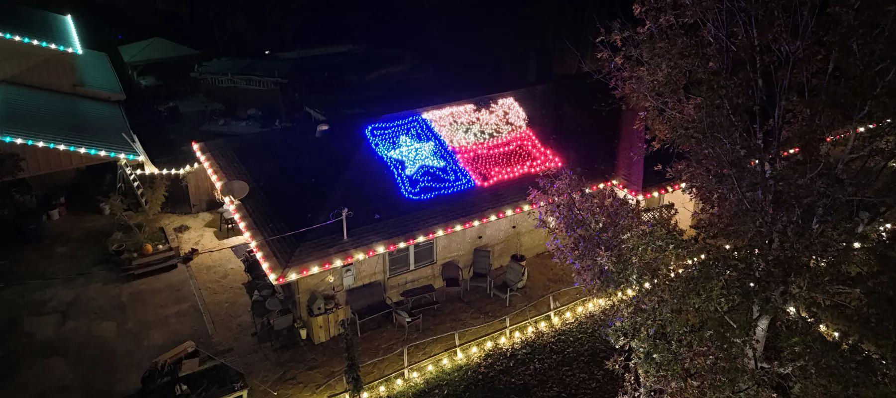 A house decorated with colorful holiday lights, including a large Texas state flag made of lights displayed on the roof at night. The porch and roofline are outlined with white and red lights.